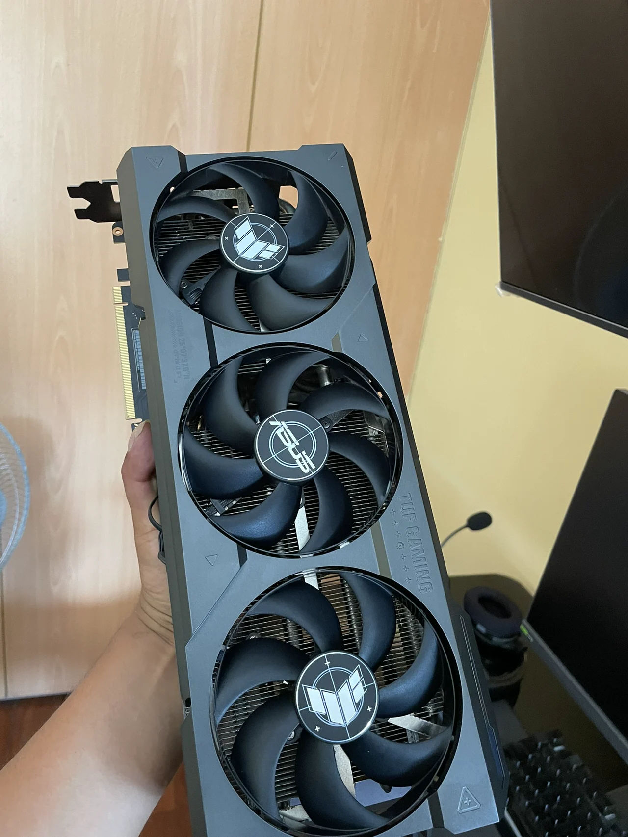 Tarjeta gráfica de tres ventiladores sostenida junto a una mesa de trabajo